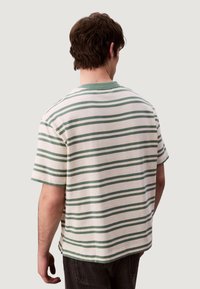 Camisa de manga corta a rayas en crema con rayas horizontales verdes. Presenta un cuello redondo y un corte relajado con una textura suave.