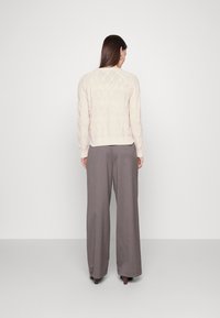 Suéter de punto trenzado crema con una textura de diamante, combinado con pantalones de pierna ancha grises, visto desde la parte trasera contra un fondo liso.
