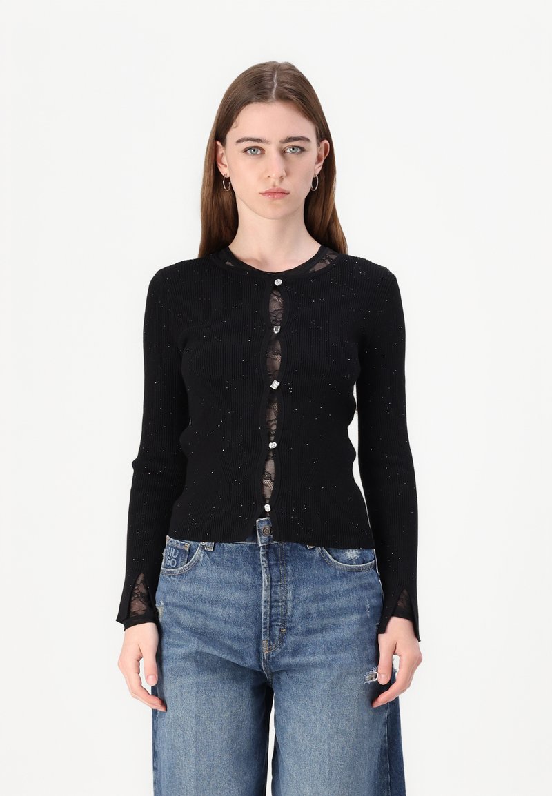 Cardigan nero a coste con maniche lunghe, caratterizzato da un pannello in pizzo e bottoni decorati. Accentuato da delicati bagliori e pizzo trasparente ai polsini.