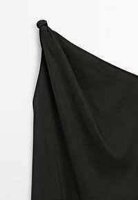 Tissu noir drapé doucement, présentant une surface texturée et un coin supérieur noué. Les bords sont bruts, soulignant la légèreté du tissu.