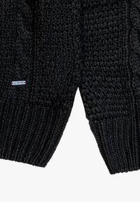 Zwarte gebreide trui met een textuurpatroon, geribbelde mouwen en een klein merklabel aan de zijkant, voorzien van een verdeling aan de onderkant.