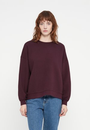 Burgunderfarget oversized genser med lange ermer, rund hals og ribbede mansjetter, kombinert med lyseblå høytlivsjeans med en glatt tekstur.