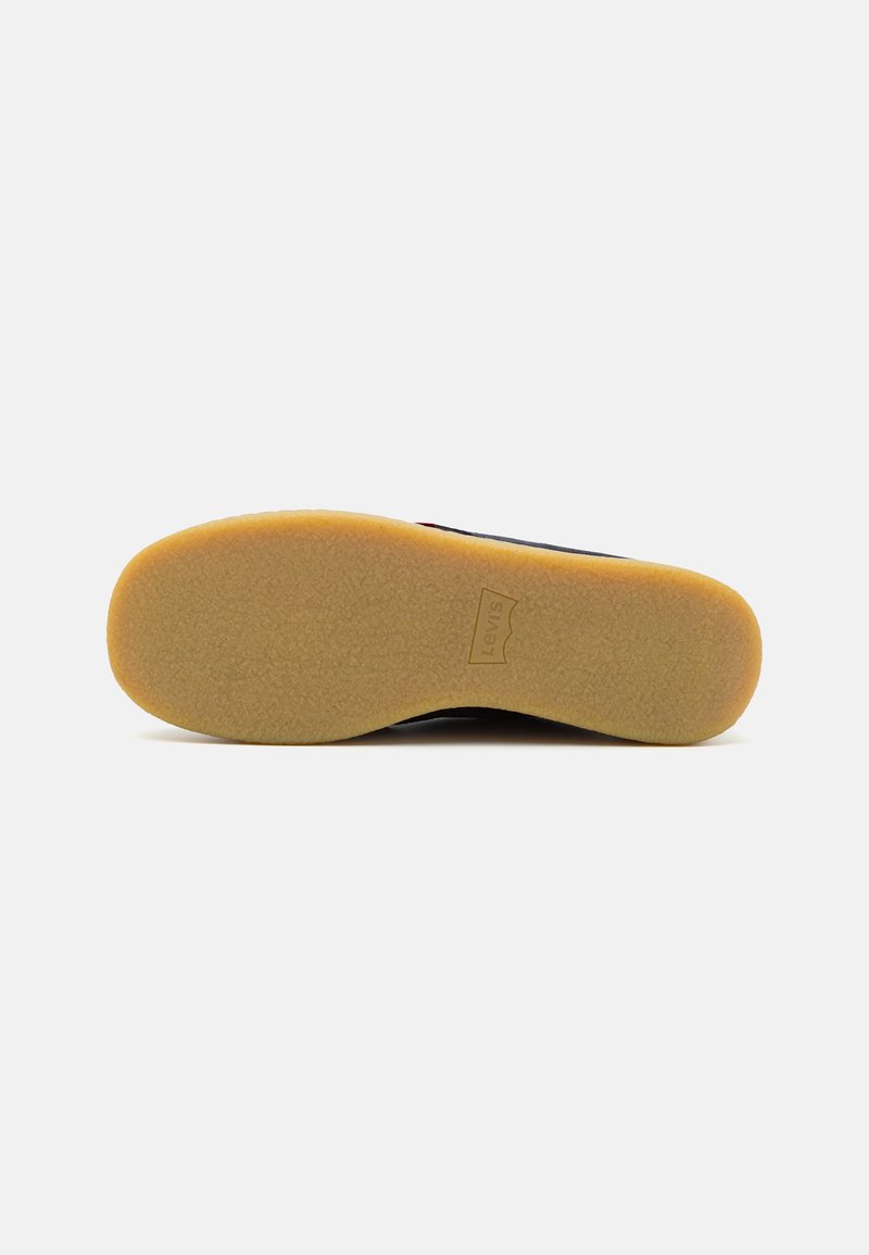 Suela de zapato negra hecha de goma con una superficie texturizada y ranurada. Los bordes reforzados y una suela beige proporcionan estabilidad y agarre.