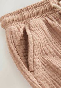 Shorts en lin rose clair avec une taille élastique et un cordon de serrage, présentant une surface texturée et des poches latérales.