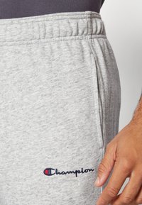 Pantaloni de trening gri din bumbac, cu un talie elastică, buzunar lateral și logo-ul brodat "Champion" în albastru și roșu în partea stângă jos.