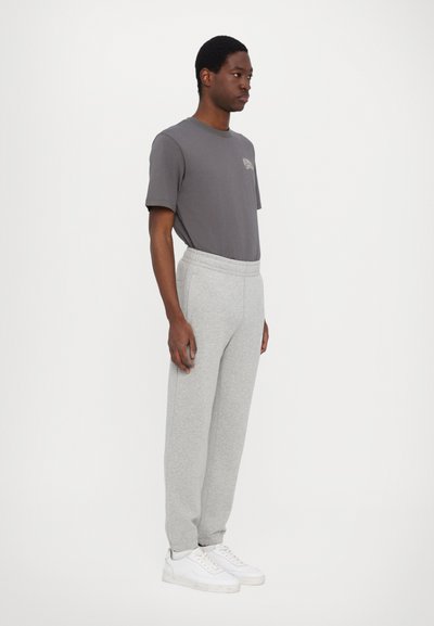 Gray cotton t-shirt with short sleeves, featuring a small chest graphic, paired with light gray sweatpants and white sneakers.