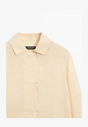 Beżowa koszula z długim rękawem, z ostrym kołnierzem i ukrytym listwą guzikową z trzema widocznymi guzikami.