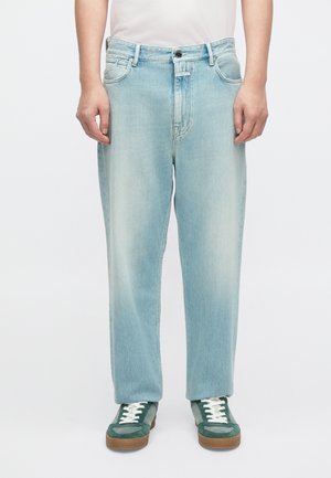 Jasnoniebieskie jeansy z denimu o luźnym kroju, z talią o średnim stanem, pięcioma kieszeniami i subtelnymi przetarciami. Połączone z zielonymi sneakersami.