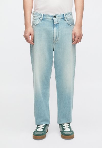 Jean en denim bleu clair à coupe décontractée, avec une taille mi-haute, cinq poches, et des détails de décoloration subtils. Associé à des baskets vertes.