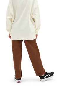 Överdimensionerad krämfärgad sweatshirt med ribbade muddar, matchad med bruna raka byxor och svarta sneakers med vita detaljer och röda inslag.