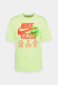 Zelené bavlněné tričko, krátké rukávy, s velkým červeným logem Nike a textem "WORLDTOUR", pod nímž jsou vytištěny názvy měst v černé barvě.