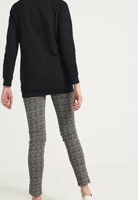 Sudadera negra de manga larga con puños acanalados, combinada con pantalones grises ajustados y texturizados que presentan un diseño estampado y un corte hasta el tobillo.