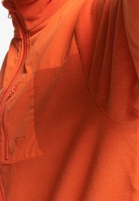 Giacca in fleece arancione con chiusura a zip, caratterizzata da una texture morbida, una tasca a toppa e un marchio discreto sul tessuto.