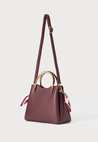 Sac à main bordeaux avec une forme structurée, ornée de quincaillerie dorée, de poignées doubles et d'un accent de foulard décoratif sur le côté.