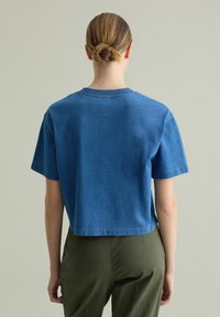 Kortgebroken, blauwe T-shirt met korte mouwen, een gladde textuur, een geribbelde halslijn en gestikte zomen, gecombineerd met olijfgroene broeken.