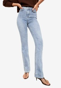 Rifľové nohavice svetlomodrej farby s vysokým pásom, priliehavým strihom, jemne vyblednuté a s dizajnom na rovné nohavice. Majú zapínanie na gombík a klasické vrecká.