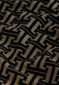 Textil negro con un patrón geométrico de formas entrelazadas en dorado y crema, con una textura aterciopelada y líneas prominentes.