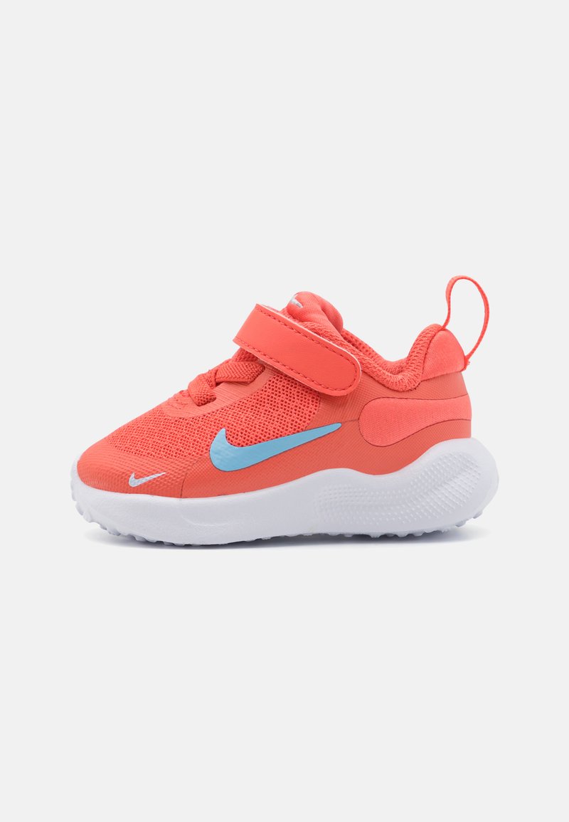 Baskets Nike de couleur corail avec une tige en mesh respirant, un swoosh bleu accentué, une sangle ajustable et une semelle en caoutchouc texturé blanche.