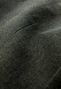 Tmavozelená látka s jemnou textúrou, diskrétnym leskom a slabými stehmi. Zblízka je zdôraznená detailnosť materiálu a hladký povrch.