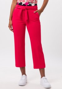 Bright pink cropped pants with a textured fabric, featuring a tied belt at the waist. Paired with white sneakers.