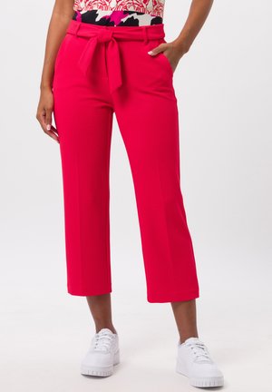 Bright pink cropped pants with a textured fabric, featuring a tied belt at the waist. Paired with white sneakers.