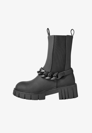 Botas Chelsea negras de piel lisa con una suela gruesa y plataforma, paneles laterales elásticos y una cadena decorativa chunky alrededor del tobillo.