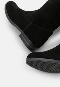 Czarne botki zamszowe za kostkę o zaokrąglonym czubku, niskim gumowym obcasie oraz teksturowanej podeszwie z wzorem zapewniającym przyczepność. Ogólnie gładka faktura.