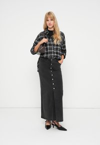 Black plaid button-up shirt paired with a black denim maxi skirt featuring front buttons and a slit, complemented by black pointed heels.