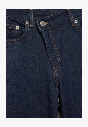 Nahaufnahme einer dunkelblauen Denim-Jeansvorderseite mit Metallknopf, Reißverschluss, Fronttaschen und orangefarbenen Steppnähten.