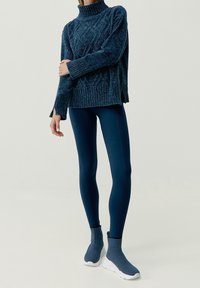 Tjock blå stickad tröja med hög krage, matchad med släta blå leggings och välsittande blå slip-on skor med vita sulor.