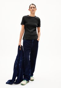 T-shirt noir à manches courtes avec une finition texturée, associé à un pantalon large en velours côtelé bleu foncé. Baskets blanches avec des accents verts.