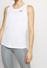 Débardeur de sport blanc avec un col rond et un logo Nike noir. Le tissu semble lisse et léger, adapté aux activités sportives.
