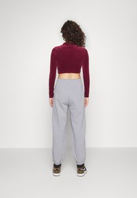 Top corto acanalado color burdeos con mangas largas, combinado con pantalones de chándal grises holgados, que presentan puños elásticos y un ajuste relajado.