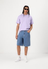 Light purple short-sleeve shirt, blue denim shorts, and white sneakers. Sunglasses add a sleek touch. Simple design and casual fit.
