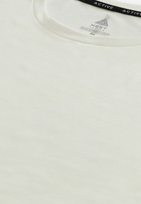 T-shirt de sport blanc à col rond avec de petites perforations et une étiquette intérieure indiquant Next Active taille medium.