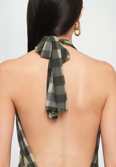 Halter-neck dress featuring a checkerboard pattern in green and black fabric, with a tied bow detail at the back and an open back design.