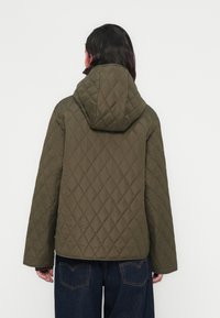 Πράσινο μπουφάν πετσετέ με κουκούλα, με μοτίβο σε σχήμα ρόμβου και φαρδιά μανίκια, συνδυασμένο με σκούρο μπλε τζιν.