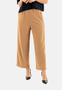 Pantalons larges couleur beige fabriqués dans un tissu lisse avec une taille élastique, présentant une coupe décontractée et une taille mi-haute.