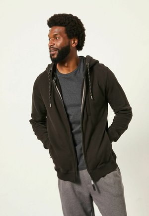 Black zip-up hoodie with gray interior lining, featuring drawstrings and front pockets, worn over a gray t-shirt and gray sweatpants.