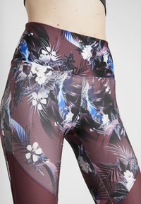 Blommönstrade leggings i texturerad mörkröd tyg med tropiska mönster i lila, blått och vitt. Hög midja med sidofickor.