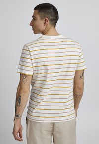 Short-sleeve white T-shirt featuring horizontal stripes in yellow and light pink, with a crew neckline and soft cotton texture.