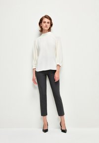 Blusa bianca a maniche lunghe con collo alto, abbinata a pantaloni grigio scuro slim-fit e décolleté nere a punta. Tessuto liscio, design minimalista.