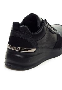 Sneaker nera caratterizzata da una combinazione di materiali sintetici lisci e perforati, con un accento di logo metallico sul tallone e suola in gomma flessibile.