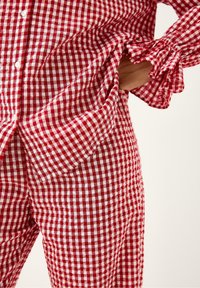 Rød- og hvidternet outfit med en skjorte med knaplukning, der har flæsekant og matchende bukser. Letvægtigt, ternet stof.