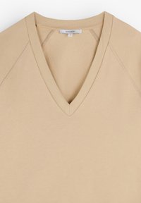 Beige V-Ausschnitt-Pullover aus strukturiertem Stoff mit Rippstrickbesatz am Kragen und an den Ärmeln. Verfügt über ein Etikett am Ausschnitt mit dem Markennamen.