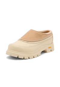 Sabot beige et fauve à enfiler avec une semelle Vibram robuste et une tige cousue, conçu pour un usage décontracté et en extérieur.