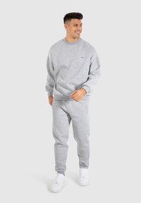 Un sweatshirt gris et un pantalon de jogging assorti en tissu doux. Le haut a un col rond et des coutures latérales, tandis que le pantalon comporte des poches latérales.