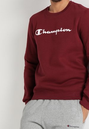 Bordeaux Champion-sweatshirt kombineret med lysegrå Champion-sweatpants, begge med mærkets hvide og røde logoer foran.