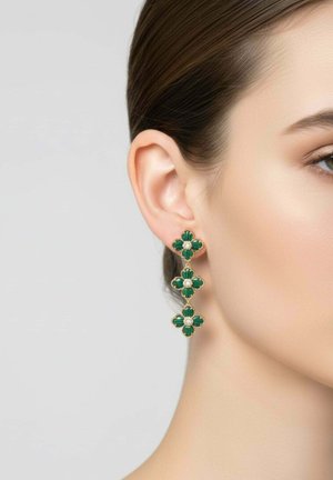 Primo piano dell'orecchio di una donna che indossa un orecchino pendente d'oro con tre ciondoli verdi a forma di fiore collegati, ciascuno con un piccolo perla al centro.