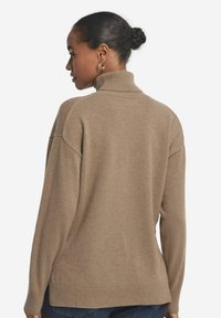 Brauner Strickpullover mit hohem Kragen, lockerer Passform und geripptem Saum. Der Stoff wirkt weich mit einer glatten Textur.